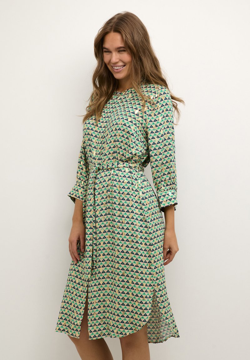 Rochie verde cu un model triunghiular, dintr-un material ușor, având mâneci lungi, brâu la talie și o fanta frontală pentru un plus de libertate de mișcare.