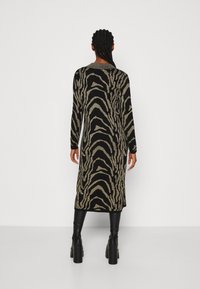 Abito nero con strisce a zigzag dorate, maniche lunghe e taglio dritto. Indossato con stivali neri fino al ginocchio, che mostrano una trama elegante.