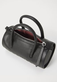 Sac à main en cuir noir avec une surface texturée, deux poignées, fermeture éclair en argent et intérieur bordeaux. Présente une forme cylindrique.