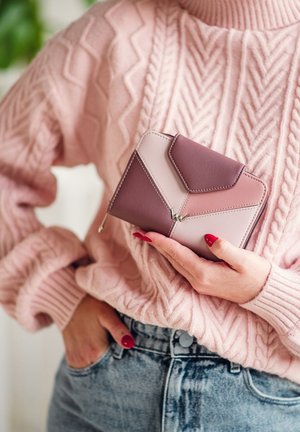 Multi-tone leather wallet featuring geometric design with pink and mauve sections. Silver hardware accent and zip closure. Hand-held against a sweater.