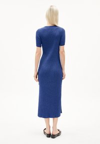 Knee-length blue ribbed knit dress with short sleeves and side slits, made from a textured fabric. Flat black sandals complete the outfit.