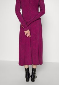 Long-sleeved, fuchsia dress with a textured diamond pattern and flared skirt, paired with high-heeled black ankle boots.