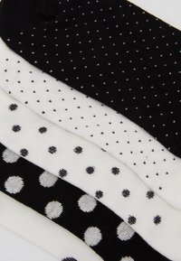 Quattro paia di calzini in bianco e nero, caratterizzati da piccoli motivi a pois e da pois più grandi, con una morbida texture lavorata a maglia.