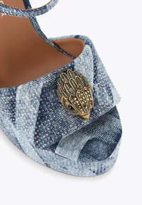 Sandalo platform in denim con un motivo a gradiente blu, finitura in tessuto testurizzato e un'accoppiatura decorativa metallica a forma di uccello.