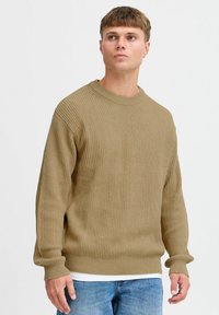 Brown ribbed knit sweater with a crew neck and long sleeves, paired with light blue jeans. The texture is soft and relaxed-fit.