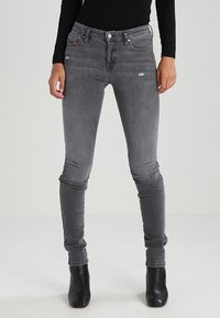 Jeans ajustados de mezclilla gris con detalles desgastados, con una cintura de altura media, cinco bolsillos y un diseño ceñido.
