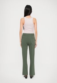 Pantaloni verzi până la talie, cu picioare evazate și două buzunare la spate. Asortați cu un top din bumbac roz deschis. Ţesătură netedă și croială ajustată.