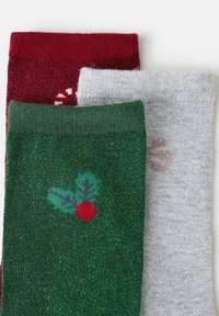 Drei Paar festliche Socken: rot mit Glitzer und Muster, dunkelgrün mit Stechpalmen-Design und hellgrau mit dezenten Schneeflocken.