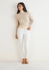 Beżowa dopasowana bluzka z golfem, białe eleganckie spodnie i jasnobrązowe baleriny. Gładka tekstura z prostym wzornictwem, bez widocznych wzorów czy akcentów.