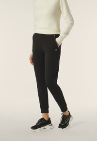 Pantaloni jogger neri con una vestibilità affusolata, tasche laterali e un piccolo logo. Abbinati a un maglione bianco e sneakers nere.