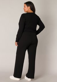 Zwarte lange mouwen top en hoge taille broek van gladde stof, met een relaxte pasvorm en subtiele stiksels. Witte sneakers.