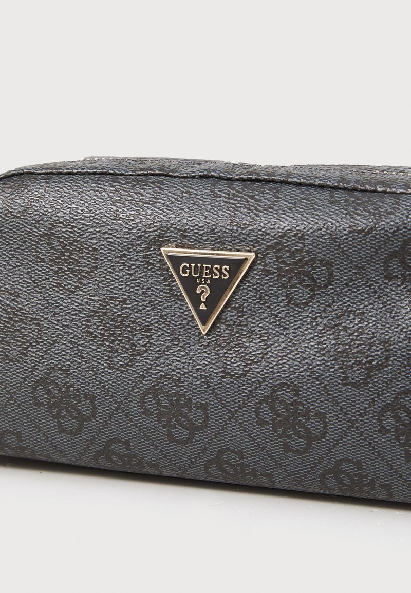 Bolsa negra texturizada con un patrón de logotipo en relieve. Presenta una placa de logotipo en tono dorado en forma de triángulo con "GUESS" y un signo de interrogación.