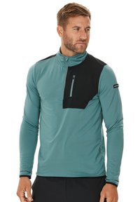 Helles türkisfarbenes Langarm-Pullover mit einer schwarzen Brusttasche. Verfügt über einen Reißverschluss und einen hohen Kragen. Hergestellt aus glattem, elastischem Material.