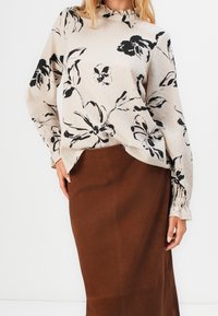 Lettet beige bluse med sort blomsterprint, rund halsudskæring med rynker, lange ærmer med samlede manchetter, parret med en brun nederdel.