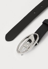 Black leather belt featuring a metallic oval buckle adorned with clear rhinestones and a cut-out design, adding a decorative accent.