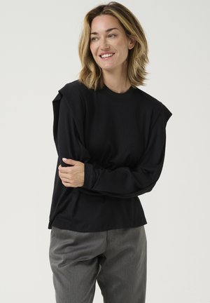 Mustmust tekstuuriga pikkade käistega shirt, millel on puffed õlad ja ümar kaelus, koos hallide kõrge vöökohaga pükstega.