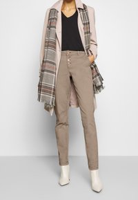 Beżowe spodnie o dopasowanym kroju, z przodem na pięć guzików, w połączeniu z jasnoróżowym płaszczem i szarym w kratkę szalikiem. Białe, kanciaste botki za kostkę.