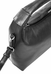 Czarna skórzana torebka o usztywnionej konstrukcji, gładkiej fakturze, z górnym uchwytem, odpinanym paskiem i srebrnymi akcentami metalowymi. Zapięcie na suwak.