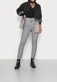 Veste boutonnée dégradée noir et gris portée sur un top en dentelle noire transparente, associée à un pantalon à carreaux gris et des bottines noires à fermeture éclair.