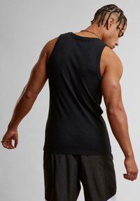 Svart ermeløs tanktop i en tettsittende stil, laget av glatt stoff, med rund hals og brede armhull, brukt sammen med svarte shorts.