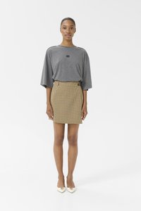 T-shirt gris oversize avec un logo au centre, associé à une jupe à carreaux jaunes avec des boutons et une coupe ajustée.