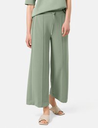 Light green wide-leg pants made of soft fabric, featuring a drawstring waistband, side seams, and a smooth texture. Paired with beige slide sandals.
