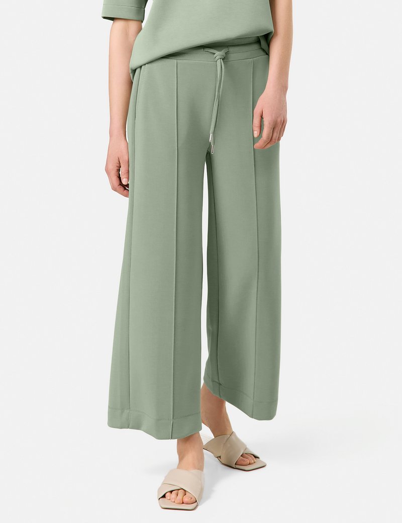 Light green wide-leg pants made of soft fabric, featuring a drawstring waistband, side seams, and a smooth texture. Paired with beige slide sandals.