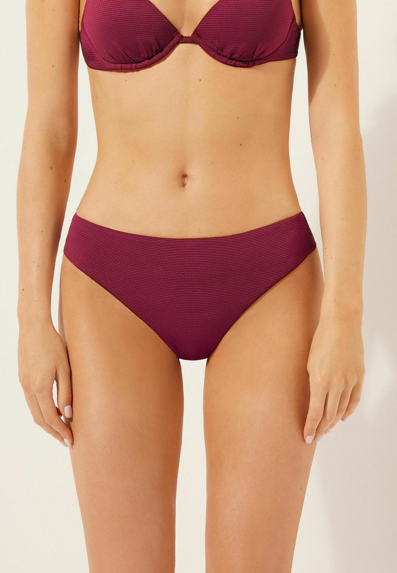 Burgundy bikiniunderdel i texturerat tyg med låg midja, som har släta kanter och en minimalistisk form.