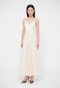 Μακρύ, κρεμ βραδινό φόρεμα από τούλι με περίτεχνη κεντημένη λουλουδένια διακόσμηση. Διαθέτει εφαρμοστό μπούστο, ντεκολτέ σε σχήμα V και λεπτές τιράντες.