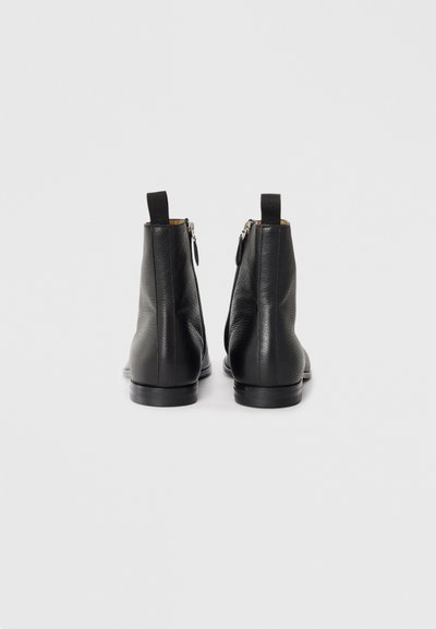 Botas de tobillo de cuero negro con un acabado texturizado, que cuentan con una cremallera trasera y una lengüeta en el talón. Suela de goma plana para mayor comodidad.