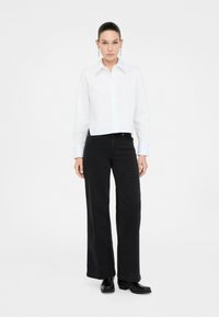 Camicia bianca corta con colletto a punta, caratterizzata da cuciture dettagliate; abbinata a pantaloni neri a vita alta e a gamba larga e a stivali neri.