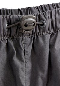 Grå elastisk midja med justerbar snodd, med rynkad tygtextur och platta sömmar. Slätt, lätt material.