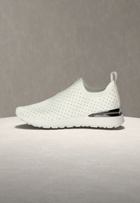Sneaker à enfiler blanc avec une tige en tricot texturé ornée de petits clous métalliques. Comprend un accent métallique sur le talon et un col rembourré.