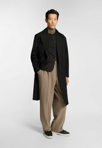 Czarny dwurzędowy płaszcz trench z wzorzystą czarną kurtką, w połączeniu z beżowymi spodniami o szerokich nogawkach i czarnymi trampkami z białą podeszwą.