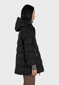 Giacca imbottita nera con cappuccio, design trapuntato e tasche laterali con zip. Realizzata in materiale leggero e resistente all'acqua.