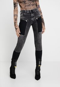 Černé a šedé džínové kalhoty s vysokým pasem, texturovanými panely a zipovými kapsami v přední části.