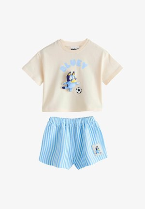 Krem majica kratkih rukava s likom psa Bluey kako udara nogom u loptu te plave kratke hlače s bijelim prugama i elastičnim pojasom s oznakom Bluey.
