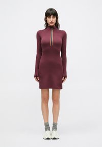 Långärmad klänning i mauve med hög krage och dragkedja i halsen med flerfärgad rand. Mjukt, figursytt material och knälång design.