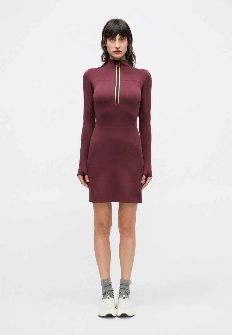 Långärmad klänning i mauve med hög krage och dragkedja i halsen med flerfärgad rand. Mjukt, figursytt material och knälång design.