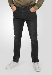 Vaqueros de mezclilla negros ajustados con una sutil textura desgastada, cierre de botón y diseño clásico de cinco bolsillos, combinados con zapatillas blancas.