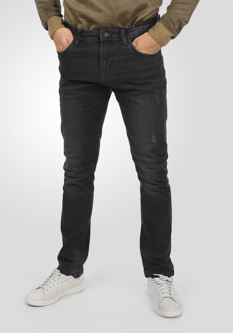 Vaqueros de mezclilla negros ajustados con una sutil textura desgastada, cierre de botón y diseño clásico de cinco bolsillos, combinados con zapatillas blancas.
