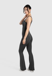 Sort sports tanktop og flagrende bukser lavet af glat, strækbart stof. Sættet har tynde stropper og en tætsiddende pasform, der er ideel til aktiv brug.