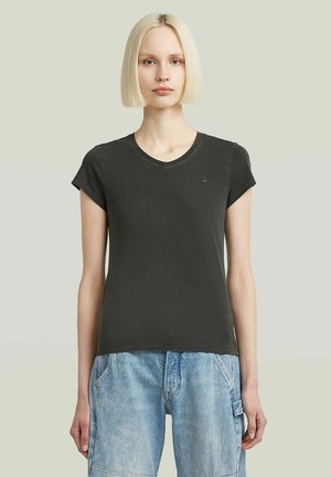 Schwarzes Baumwoll-T-Shirt mit kurzen Ärmeln, V-Ausschnitt und einem kleinen Logoakzent auf der Brust. Kombiniert mit blauen Jeansshorts.