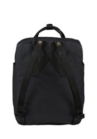 Sac à dos noir de forme rectangulaire, fabriqué en tissu durable. Présente des bretelles surpiquées et des accents de bouton sur le dessus.