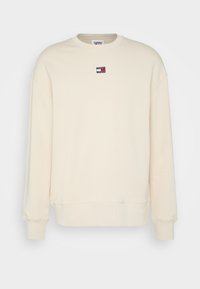 Beige long-sleeve crewneck sweatshirt with ribbed cuffs and hem, featuring a small Tommy Jeans logo patch on the chest.
