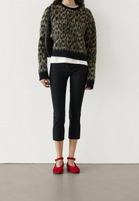 Sveti z leopardovim vzorcem s črnimi robovi, belim pod njim, v kombinaciji s črnimi skrajšanimi hlačami in rdečimi balerinkami z gležnjarji. Priložnostna oblačila.