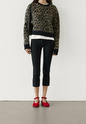 Sweter w panterkę z czarnym wykończeniem, biały top pod spodem, zestawiony z czarnymi spodniami 3/4 i czerwonymi balerinkami na kostkę. Casualowy outfit.