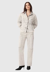 Zestaw dżinsowej kurtki i spodni w jasnoszarym kolorze z postrzępionymi krawędziami i tonującym przeszyciem, charakteryzujący się luźnym krojem i detalami w postaci kieszeni naszywanych.