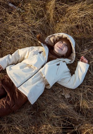 White padded jacket with a hood, featuring a star detail and front zipper, paired with brown quilted pants, on a grassy surface.