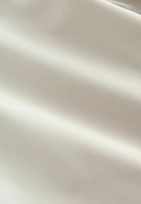Tissu lisse de couleur crème avec de fines côtes horizontales et de doux plis créant des ombres douces et des reflets.